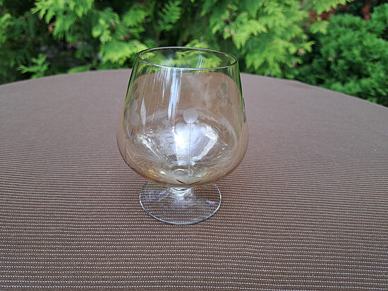 Konjaka glāze uz kājiņas, dzeltenīga lustra, puķu gravēšana. Tilpums 225ml. Diam. 7cm (Stikla gl 478)